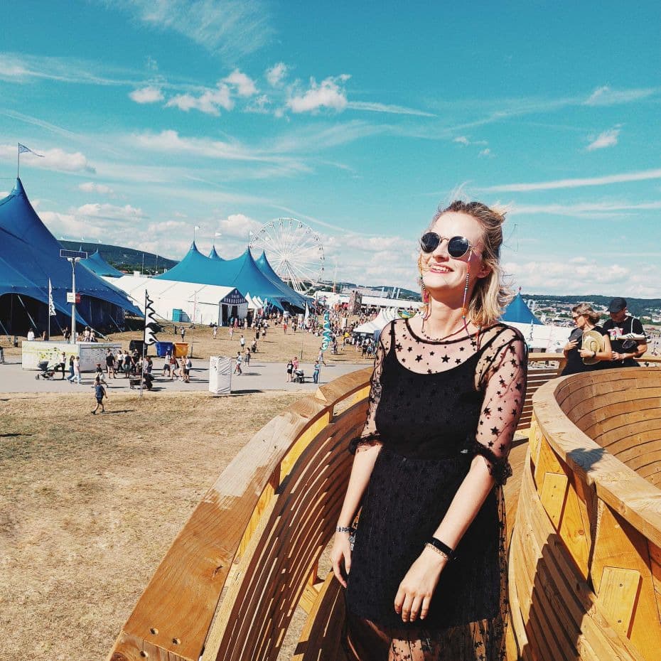Ania na festiwalu muzycznym Blondynka w okularach przeciwsłonecznych na tle namiotów festiwalu muzycznego i niebieskiego nieba